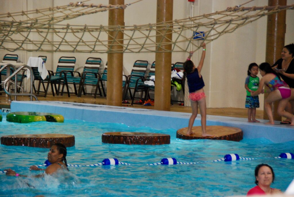 girl using ropes and floating logs to get across pool