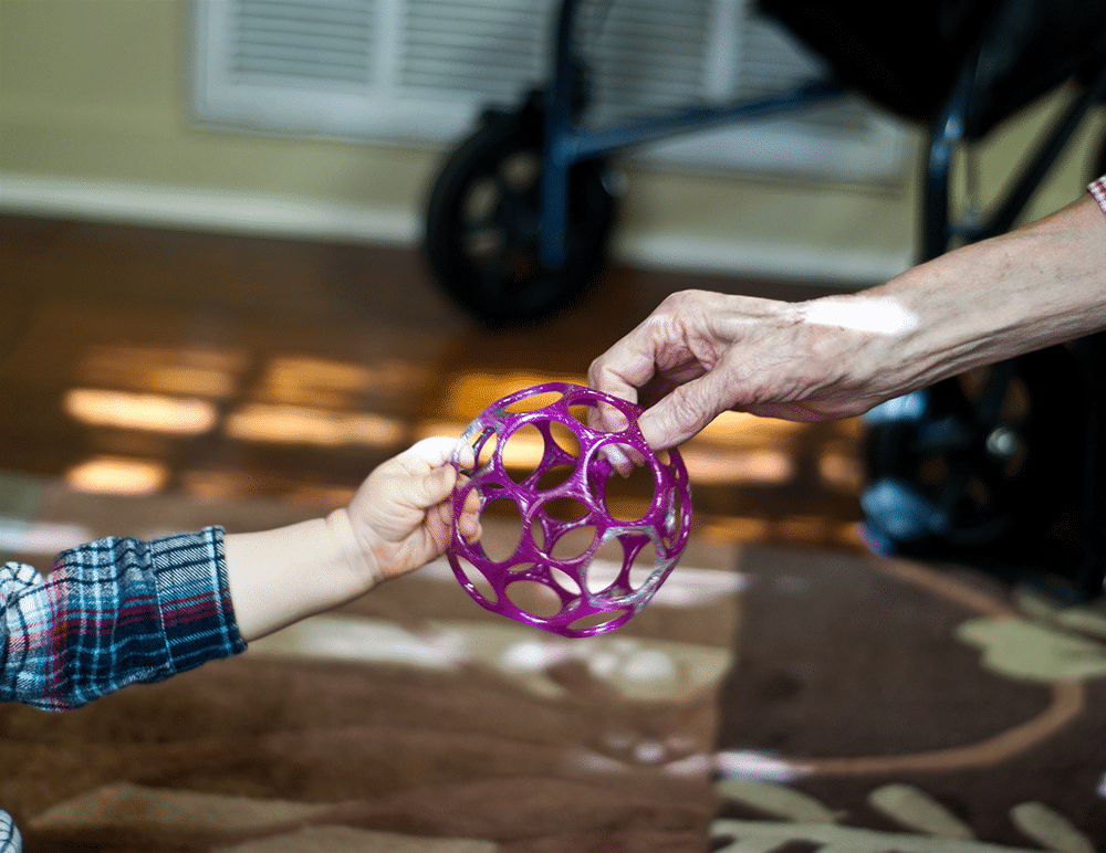 Older hand giving toy to toddler hand - baby travel hacks