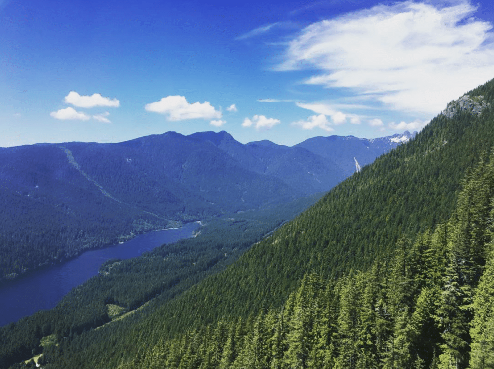 Grouse mountain, shown from above. Pine trees, mountains, clouds, and a river loom in the distance. vancouver with kids how to spend the best long weekend family travel