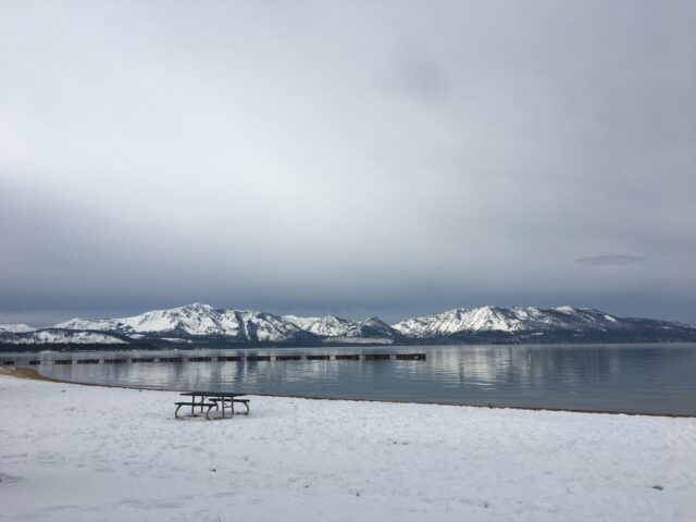 Image of Lake Tahoe, at ground level. Snow covers the ground and distant mountaintops, while the sky is overcast. 7 Not To Miss Things To Do In South Lake Tahoe With Kids family travel