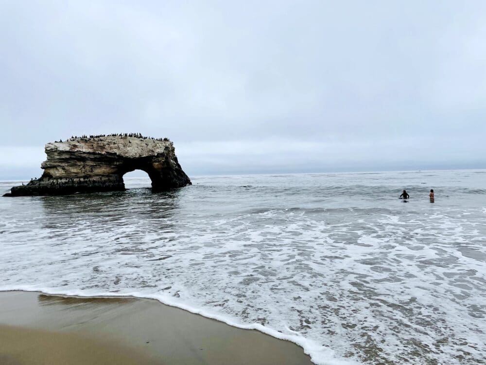 Beach, on an overcast day, with a rocky arch on the left side. Best things to do with kids in Santa Cruz family travel 