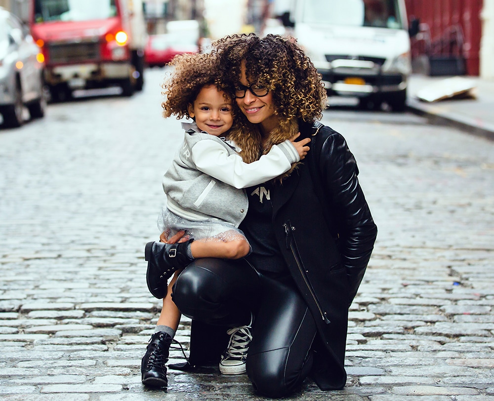 A trendy mom in black clothes poses with her preschooler on a cobblestone street. Travel hacks for moms.