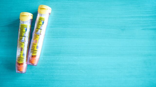 two epinephrine auto-injections, against a baby blue backdrop. managing food allergies while on vacation