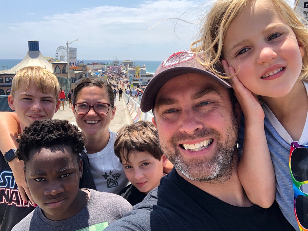 Travel tips for helping kids with vacation anxiety. Two parents and four kids stand on a pier in California during their vacation.