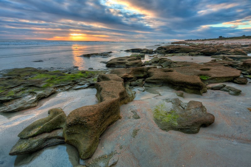 rocks over ocean and a sunset filtered by clouds - top 5 beaches in St. Augustine for kids