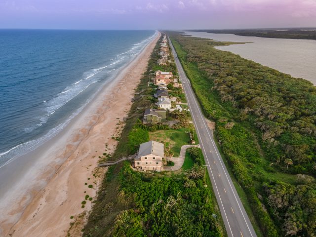 beach by strip of green land with houses - 