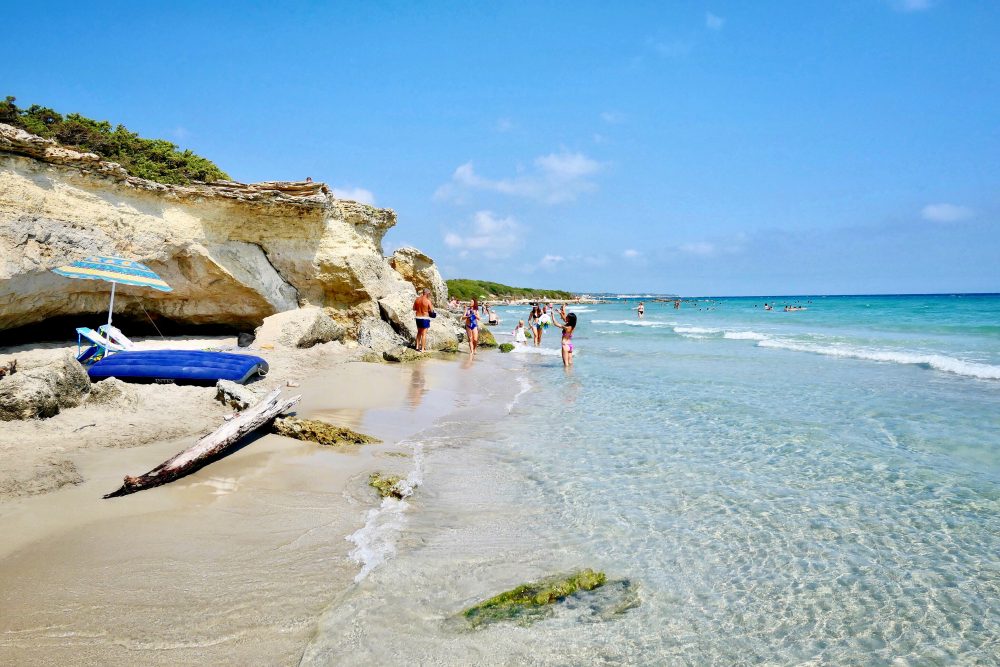 Beachgoers walk the smooth sands of Baia Dei Turchi’s rocky coast.