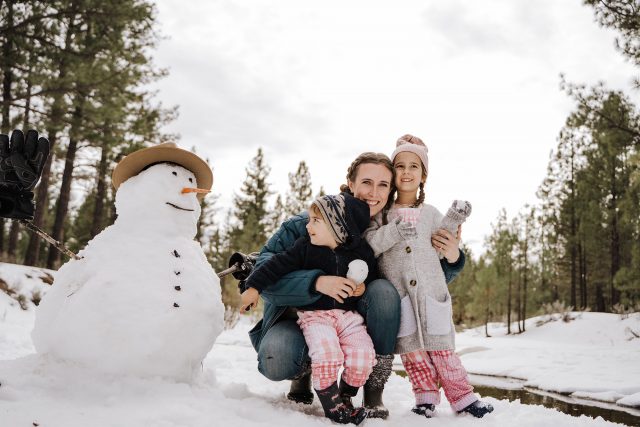 A mom and two daughters playing in the snow. They are bundled up in hats and coats for cold weather. 