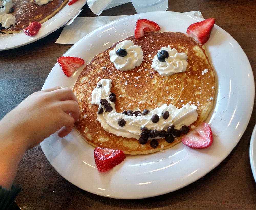 A pancake with a whipped cream smiley face and strawberries. The Pancakery is a kid-friendly place to eat on the Gulf coast.