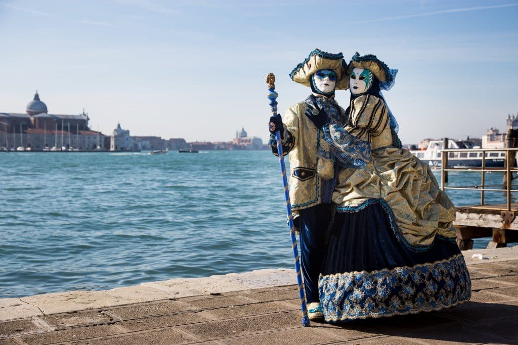 Two consumed people hug next to a canal during Carnevale di Venezia.// Where To Celebrate Carnevale In Italy With Kids
