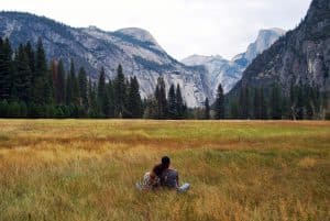 A couple sits in a field, gazing at the mountains. Sustainable travel.