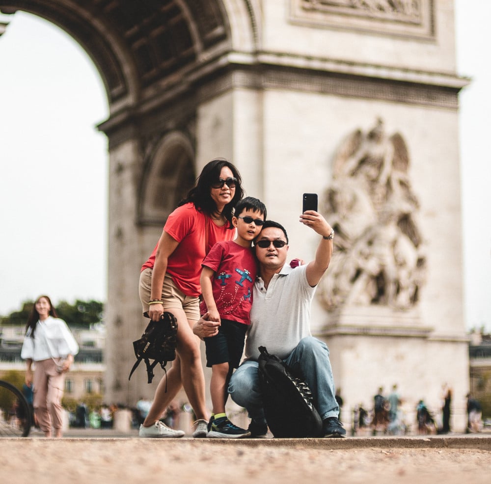 A family takes a selfie together in front of the Arc de Triomphe while on vacation. 