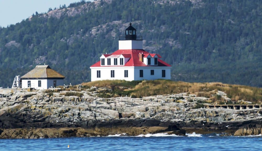 Egg Rock lighthouse on a sunny afternoon with Acadia National Parks Cadillac Mountain behind it, in Bar Harbor Maine