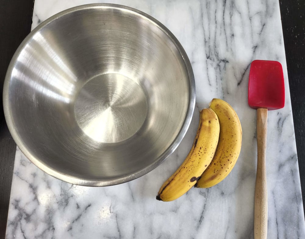A stainless steel mixing bowl, a spatula, and bananas