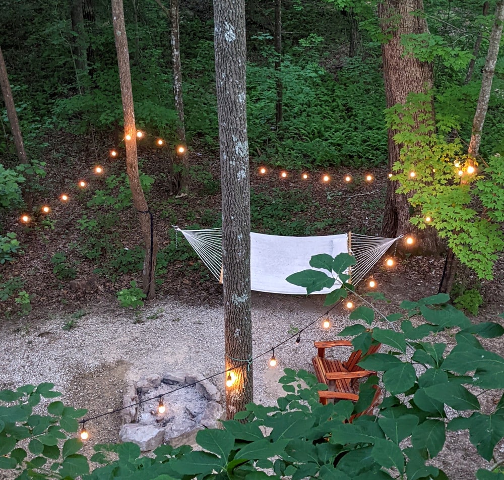 A hammock, Adirondack chairs, and string lights around a firepit