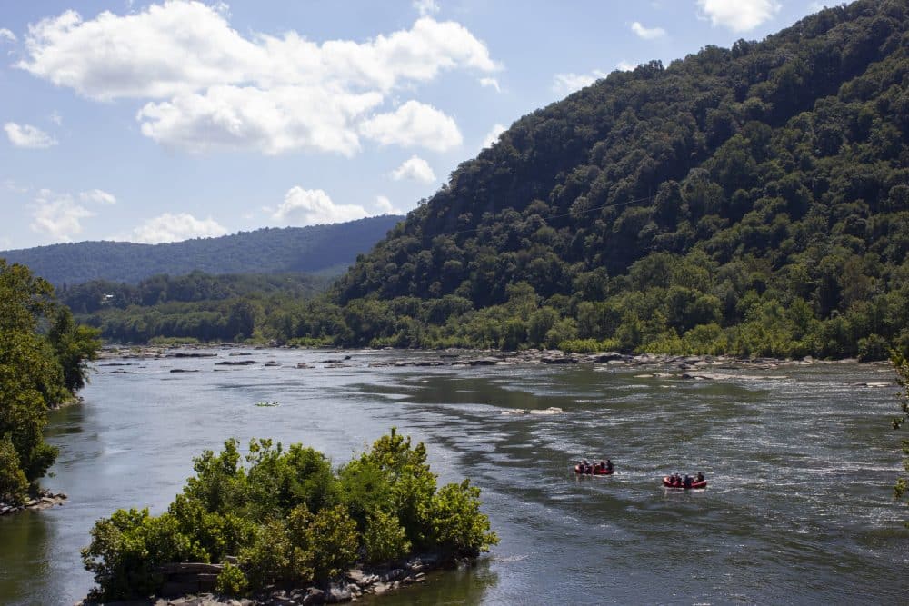 Broad river with two rafting boats and mountain in the background