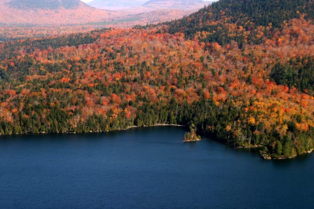 Vibrant fall foliage reflecting in Jordan Pond with the Bubbles mountains in the background at Acadia National Park