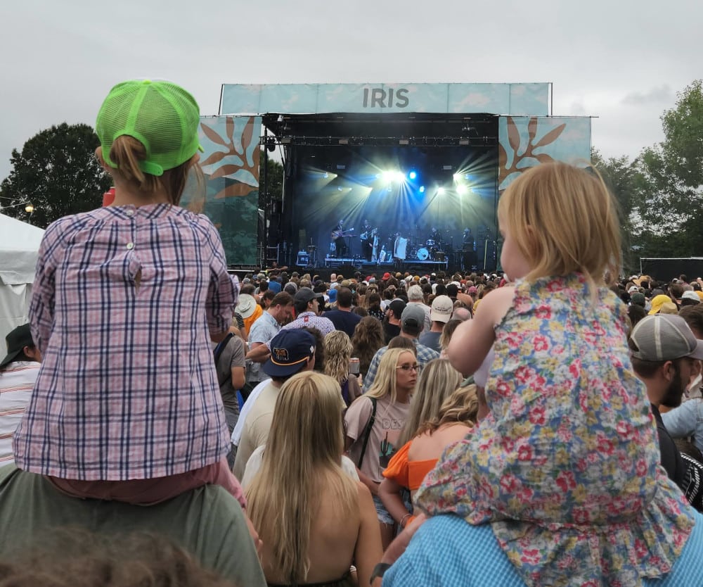 Two little girls sit on their dads' shoulders during a performance at Moon River Festival
