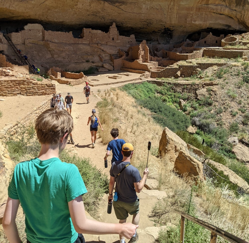 Visitors hike down a rocky trail toward Long House, part of a tour at Mesa Verde National Park