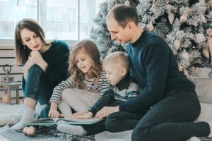 A family reading books next to a Christmas tree.