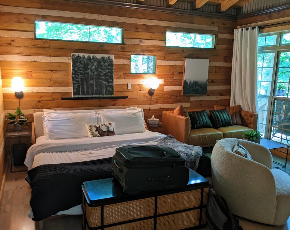 A cabin room with wood plank walls, a comfy-looking queen bed with white sheets, and a modern orange loveseat. Terralodge Treehouses in Monteagle, TN.