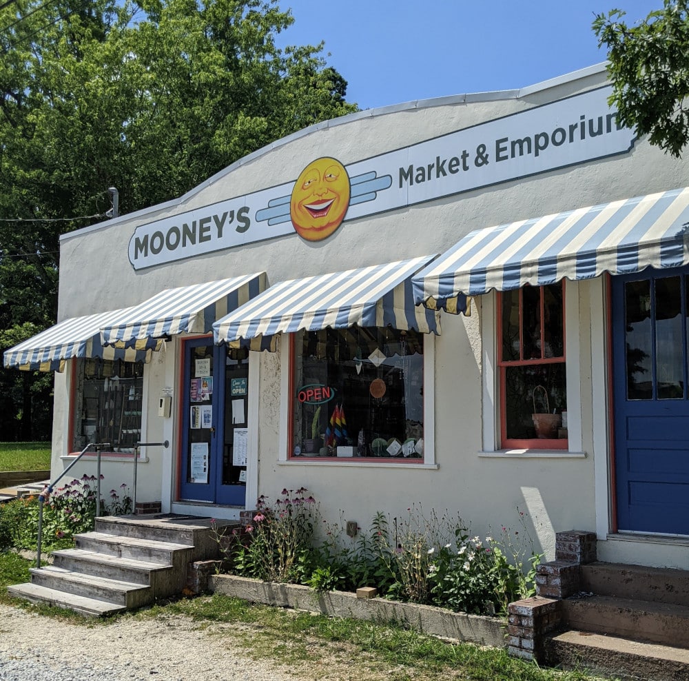 A small, off-white stucco building with green-and-white awnings. Moonies Market in Monteagle, TN.