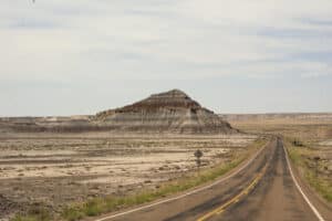 A two-lane road leading from the Painted Desert to the Petrified Forest. A striped hill is in the near distance.