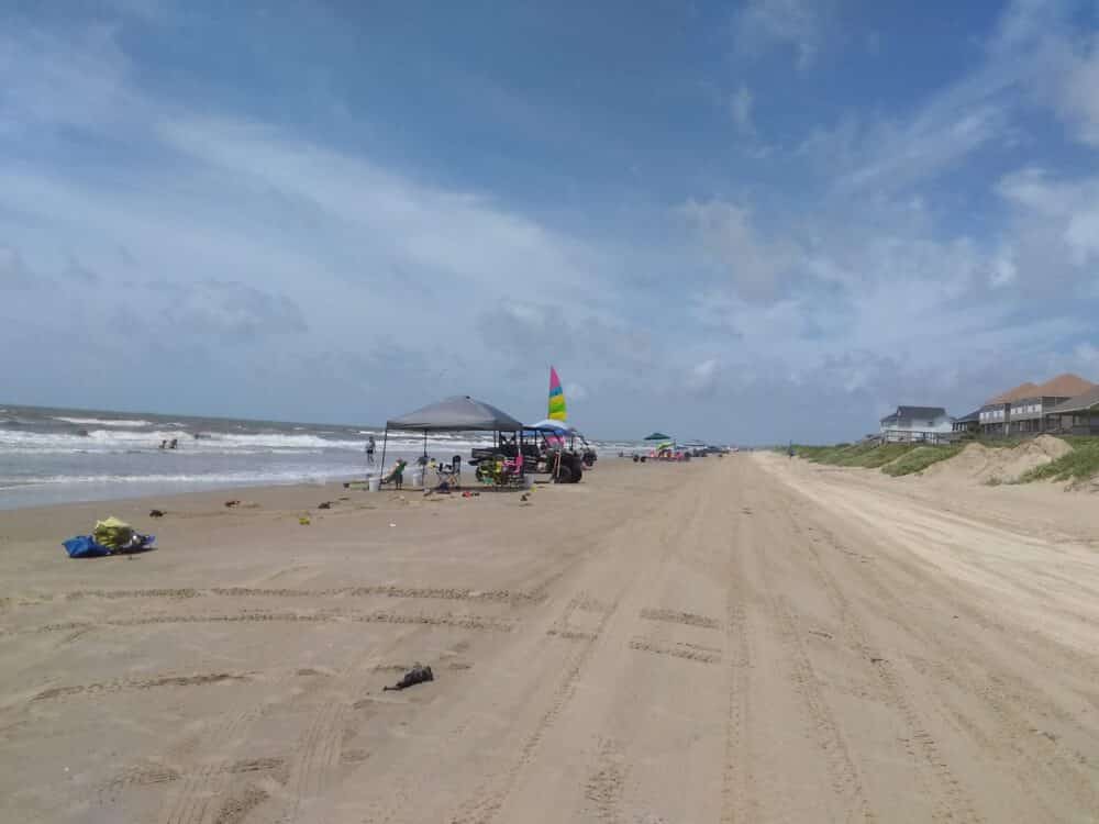 A blue sky with wispy white clouds is over a long stretch of sandy beach with very few people. Best Beaches in Galveston For Families