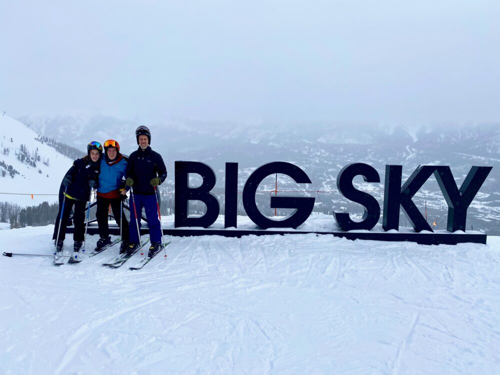 three people standing next to big sky sign - What To Do In Big Sky Montana