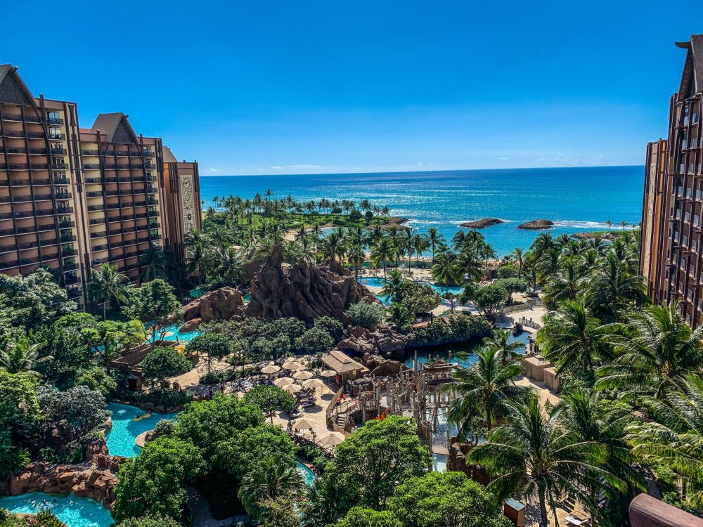 hotel towers surround lush green plants over blue pools - Best Oahu Resorts For Families