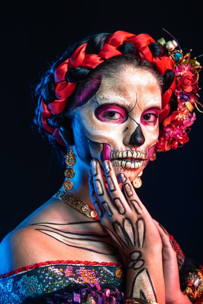 A woman with La Catrina makeup and a wreath of red flowers.
