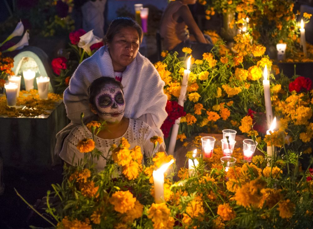 A mom and her daughter in front of an altar decorates in yellow marigolds and glowing tea lights.