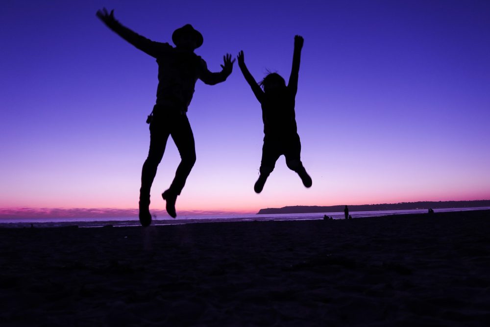 Photo of 2 people jumping in the air at the Coronado Beach, in San Diego.