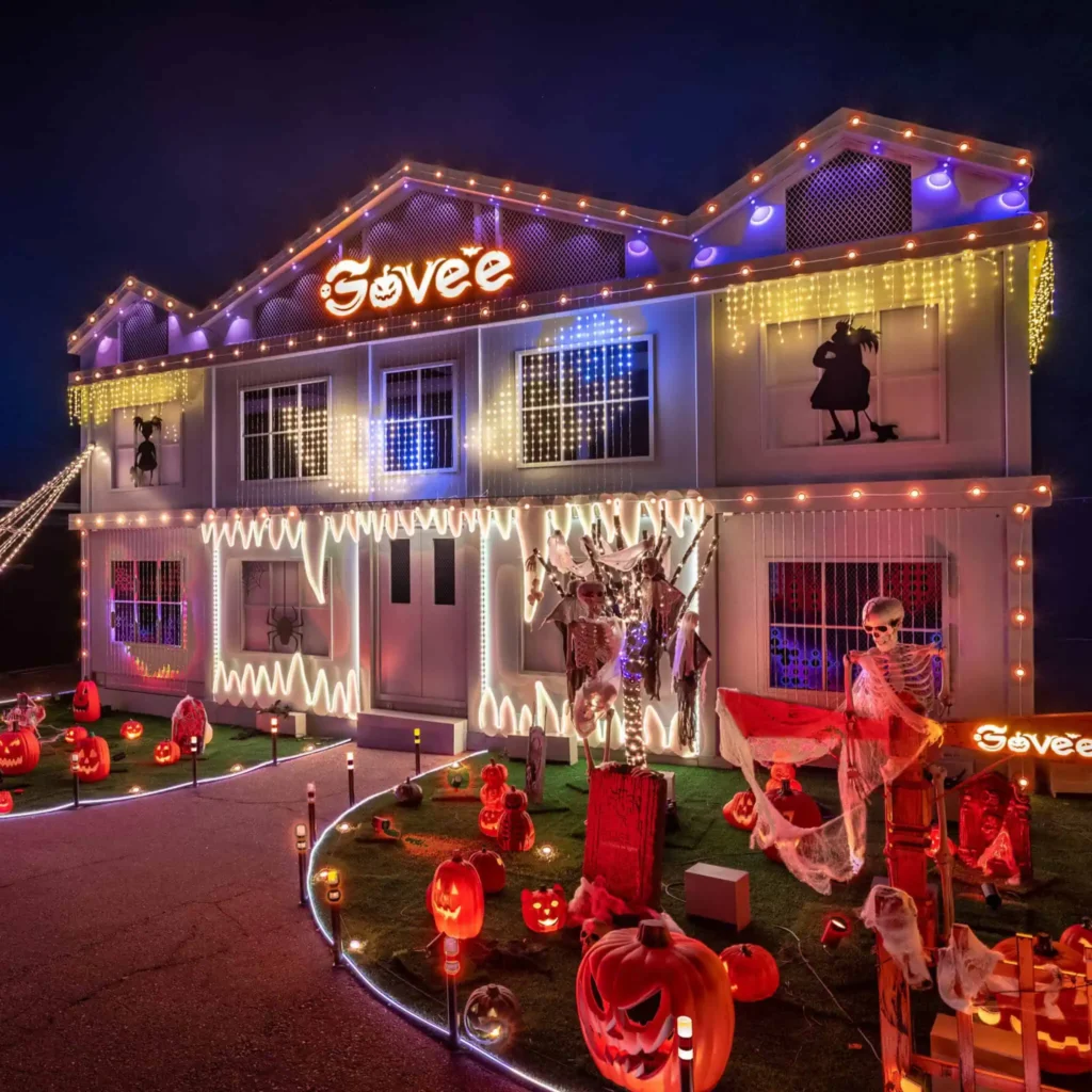 two story house lit up for holidays with pumpkins in front
