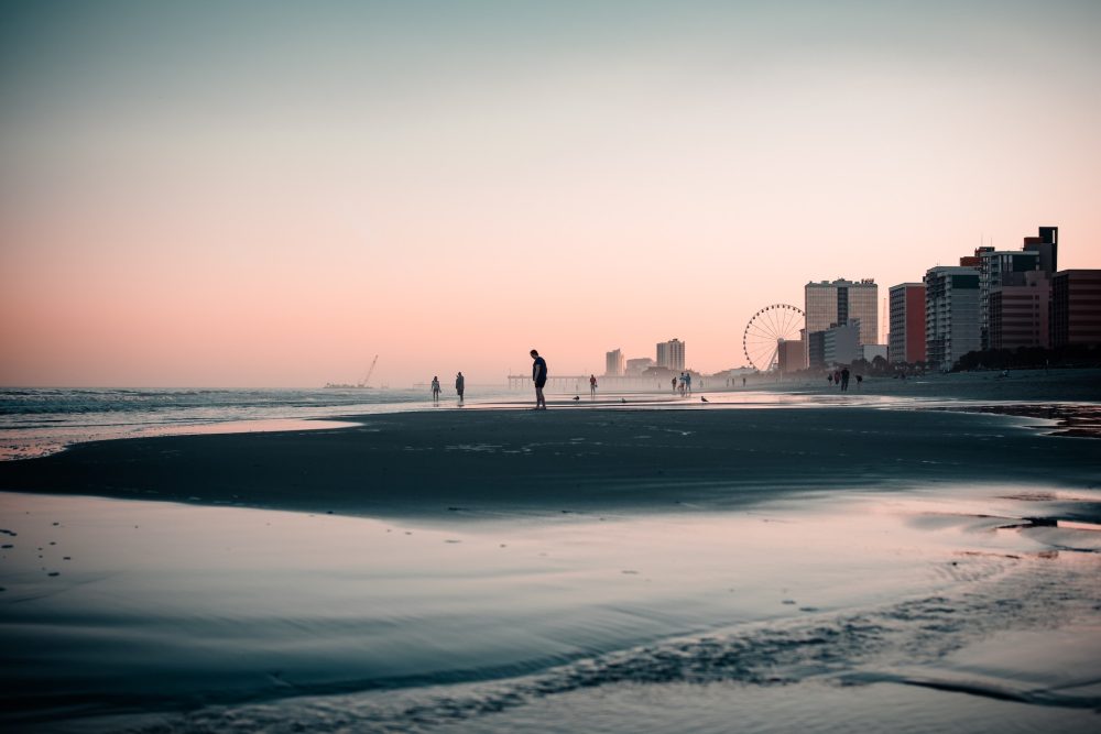 Family walking along Myrtle Beach with Skywheel in the background - best family beach vacations in October