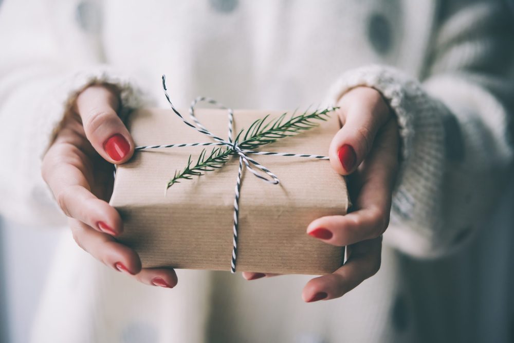 close up of a woman's hands holding a gift wrapper in brown paper with a pine twig on top