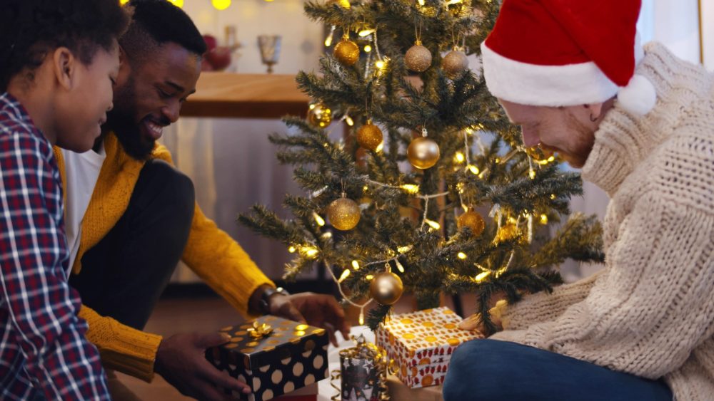 Portrait,Of,Diverse,Gay,Male,Couple,With,Preteen,Son,Decorating diverse family exchanging gifts under a tree