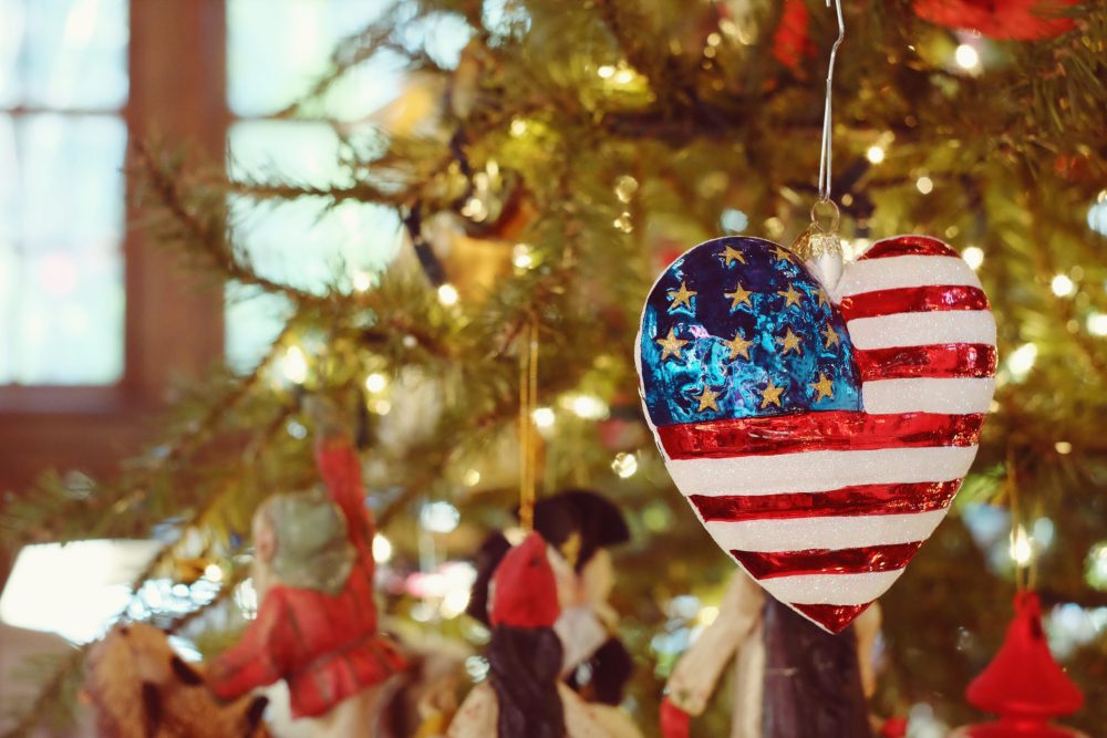 Red, white and blue heart shaped ornament on a green fir tree.