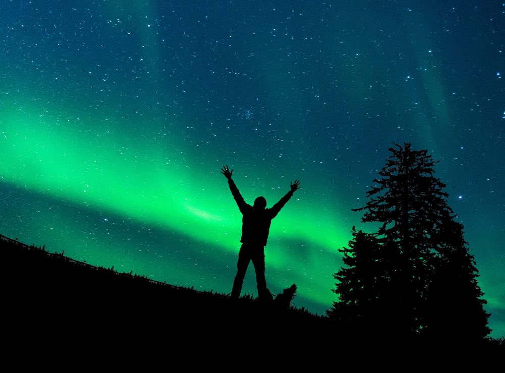 Photo of person standing under the northern lights in Alaska