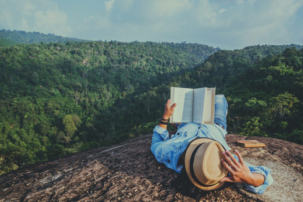 Man reads a book on a mountain overlooking a forest