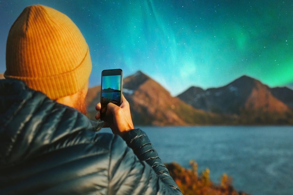 man in a knit cap photographs the neon green auroa borealis