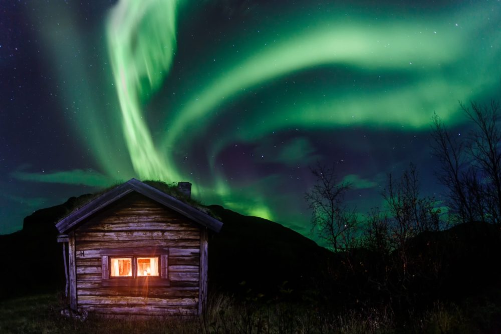 swirling neon green aurora borealis above a cozy log cabin