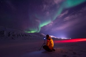 person in chilly arctic landscape photographing the northern lights