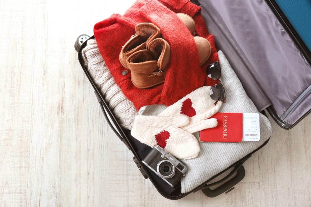 suitcase packed with cozy knits, boots, and a passport