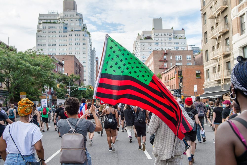 July 19th, 2020 brought hundreds of thousands onto the streets in protest in NYC. This is a picture of many of them- flying a US flag that is died black, red and green. @Shutterstock