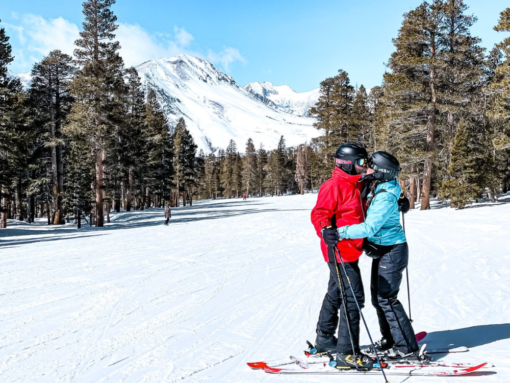 a man and woman embrace on skis and kiss