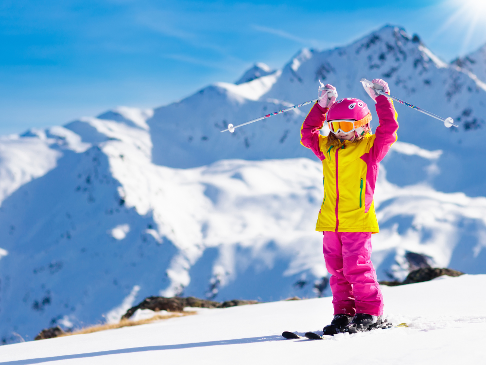 a little girl cheering because she is about to ski on a snowy mountain.