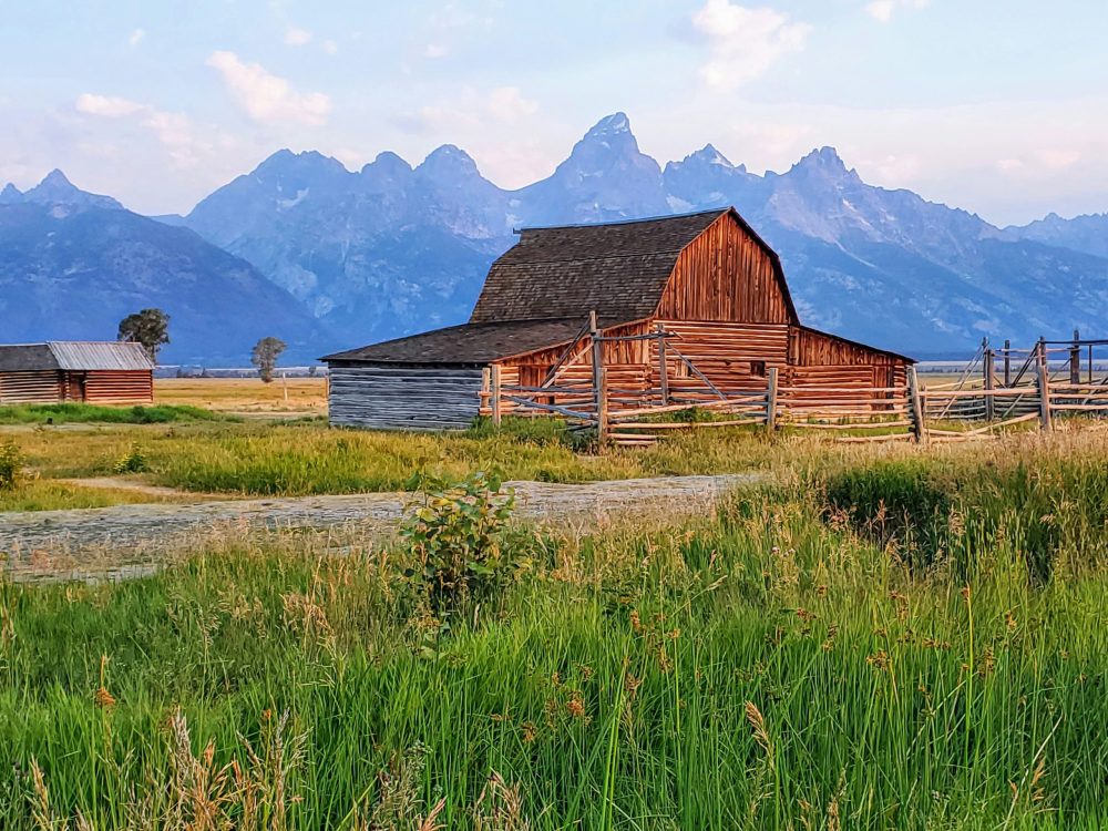 Views of the Grand Tetons and a red barn. 