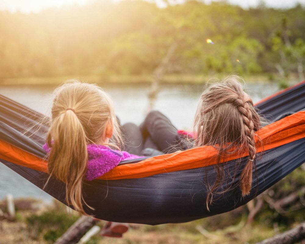 Two sisters swinging in a hammock overlooking the water.