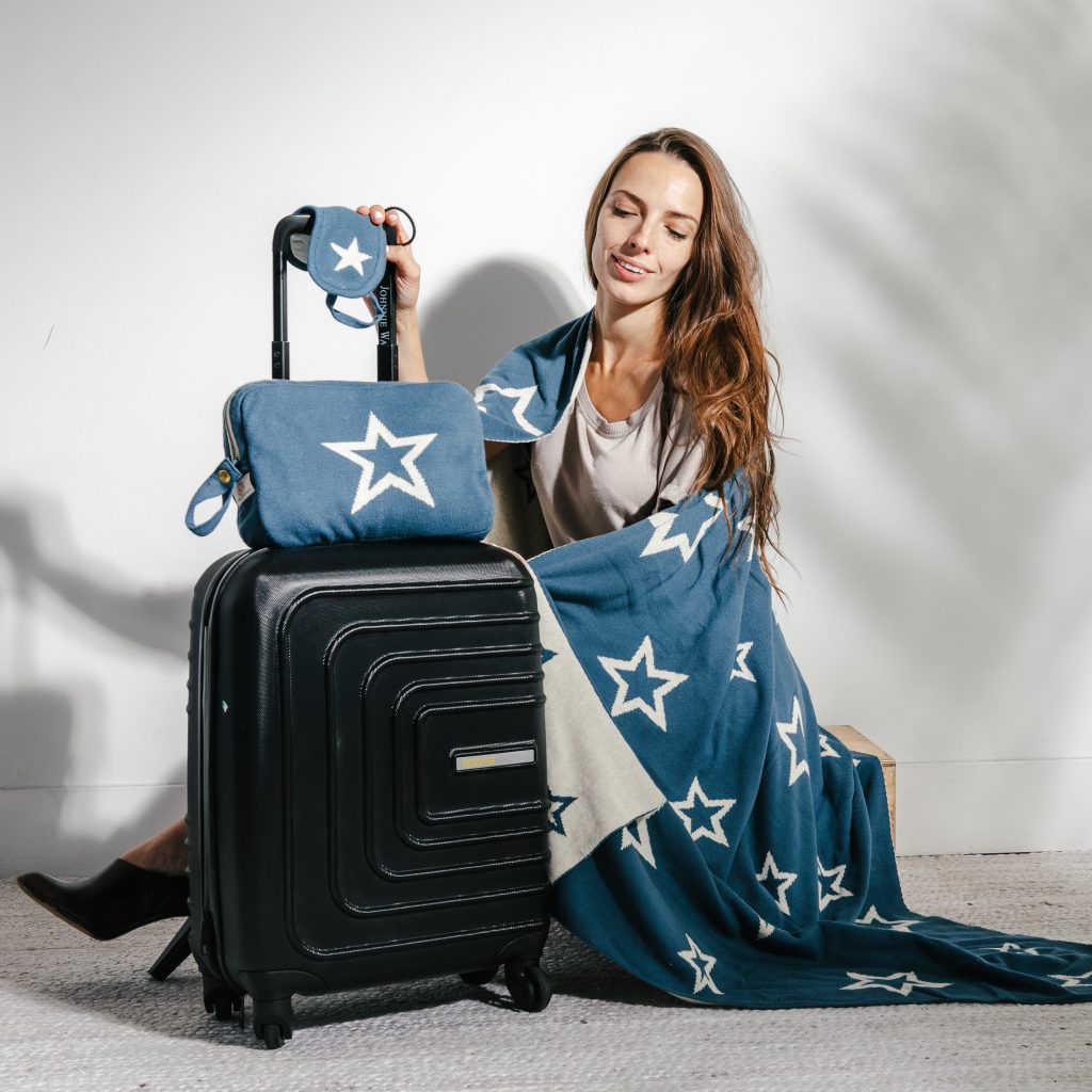 woman sitting by black suitcase covered in blue blanket with white stars